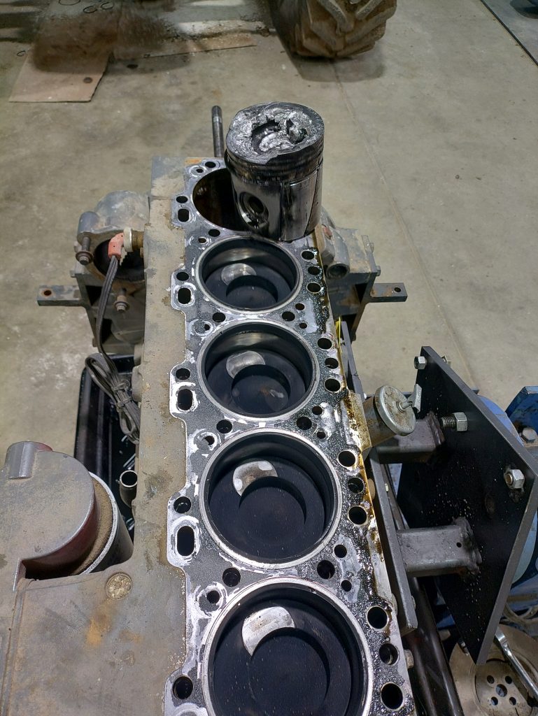 Agricultural diesel engine block showing piston damage after valve failure and timing issue